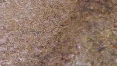 Top view, Gentle water flows over the sand, revealing beautiful textures and shimmering reflections in a serene setting. Close up. Slow motion.
