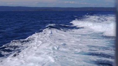 Close-up of dynamic foamy sea waves crashing and raging in the Aegean Sea. Texture of dynamic, turbulent, foamy waves created by boat motor while moving, energetic movement of water on sea background.