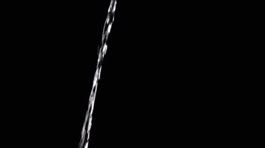 Thin Stream Of Water Pouring On Black Background. Close-up, slow motion. A clear stream of water flows down into empty space. Splashes. Abstract, texture, lighting. Clean water.