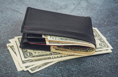 black leather wallet with banknotes lying on a rustic concrete background