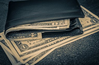black leather wallet with banknotes lying on a rustic concrete background
