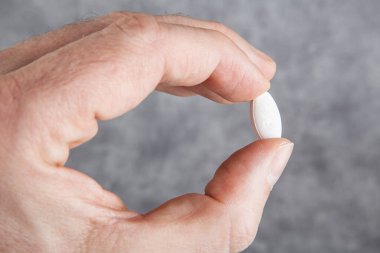 Adamın eli gri arka planda beyaz hap tutuyor. İlaca odaklan.