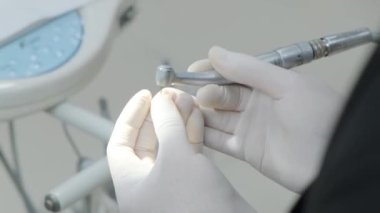 Diş hekimi, diş kliniğinde takmak için dişin boyutunu ayarlar. Beyaz eldivenli dişçi ekipmanlarıyla ameliyata hazırlanıyor..