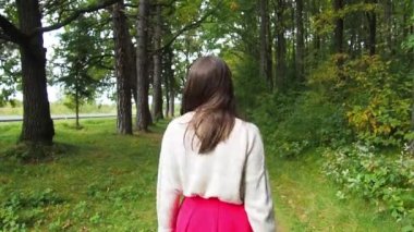 Genç bir kızın arka görünüşü uzun siyah saçları düzeltir. Gri kazaklı ve kırmızı etekli güzel bir kadın güneşli bir sonbahar gününde ormanda poz veriyor. Ormanda yürüyor ve dinleniyorum..