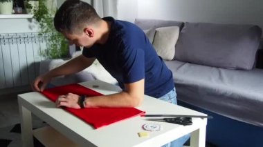 Hands of experienced worker in the handmade industry, performing cutting tasks on red fabric, on a white surface, the beginning of red hat production. Homemade sewing. Working tailor. Christmas hat.
