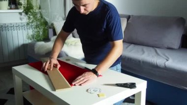 Hands of experienced worker in the handmade industry, performing cutting tasks on red fabric, on a white surface, the beginning of red hat production. Homemade sewing. Working tailor. Christmas hat.