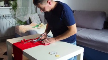 Hands of experienced worker in the handmade industry, performing cutting tasks on red fabric, on a white surface, the beginning of red hat production. Homemade sewing. Working tailor. Christmas hat.
