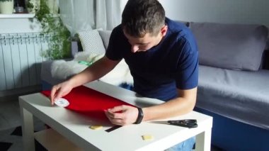 Hands of experienced worker in the handmade industry, performing cutting tasks on red fabric, on a white surface, the beginning of red hat production. Homemade sewing. Working tailor. Christmas hat.