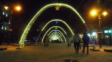 Ivano-Frankivsk, Ukrayna - Aralık 2021: Ukrayna 'nın İvano-Frankivsk kentinde kış tatilleri sırasında pek çok insanla birlikte gece parlak ışıklı yılbaşı dekoratif kemerlerinin görüntüsü. 