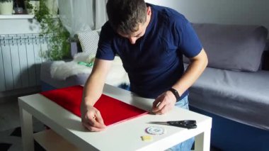 Hands of experienced worker in the handmade industry, performing cutting tasks on red fabric, on a white surface, the beginning of red hat production. Homemade sewing. Working tailor. Christmas hat.