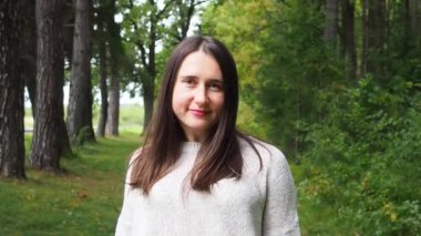 Gri kazak giyen genç kız uzun siyah saçları düzeltir. Güneşli bir sonbahar gününde ormanda poz veren bej renkli kazaklı güzel bir kadın. Ormanda yürüyor ve dinleniyorum..