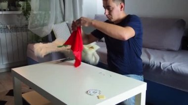 Hands of experienced worker in the handmade industry, performing cutting tasks on red fabric, on a white surface, the beginning of red hat production. Homemade sewing. Working tailor. Christmas hat.