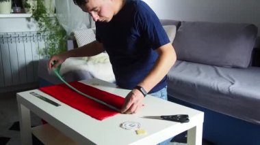 Hands of experienced worker in the handmade industry, performing cutting tasks on red fabric, on a white surface, the beginning of red hat production. Homemade sewing. Working tailor. Christmas hat.