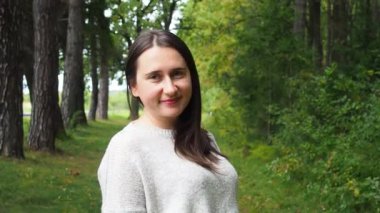 Gri kazak giyen genç kız uzun siyah saçları düzeltir. Güneşli bir sonbahar gününde ormanda poz veren bej renkli kazaklı güzel bir kadın. Ormanda yürüyor ve dinleniyorum..