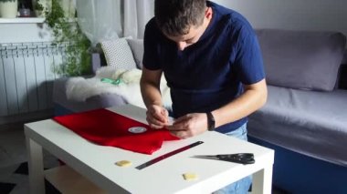 Hands of experienced worker in the handmade industry, performing cutting tasks on red fabric, on a white surface, the beginning of red hat production. Homemade sewing. Working tailor. Christmas hat.