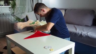 Hands of experienced worker in the handmade industry, performing cutting tasks on red fabric, on a white surface, the beginning of red hat production. Homemade sewing. Working tailor. Christmas hat.