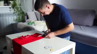 Hands of experienced worker in the handmade industry, performing cutting tasks on red fabric, on a white surface, the beginning of red hat production. Homemade sewing. Working tailor. Christmas hat.