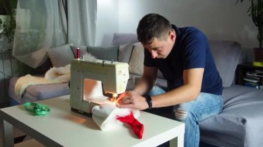 El yapımı sanayide deneyimli genç bir işçi dikiş makinesine kırmızı kumaş dikiyor, Noel Baba kırmızı şapkası üretiyor. Ev yapımı dikiş. Çalışan terzi. Noel şapkası. Kapat..