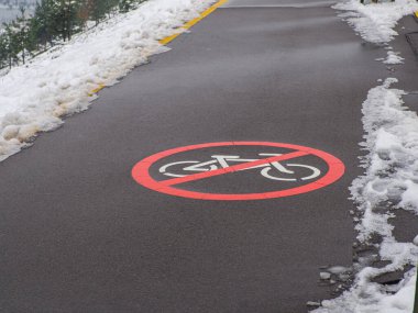 Yol işaretli bölüm bisikletçilerin hareketlerini düzenliyor. Bisiklete izin yok. Dairesel beyaz ve kırmızı trafik işareti. Gri asfalt üzerine biraz karla boyanmış beyaz bisiklet sembolü. İşaretler çizildi