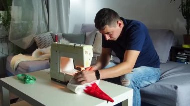El yapımı sanayide deneyimli genç bir işçi dikiş makinesine kırmızı kumaş dikiyor, Noel Baba kırmızı şapkası üretiyor. Ev yapımı dikiş. Çalışan terzi. Noel şapkası. Kapat..