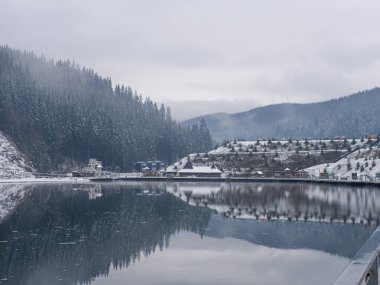 Bukovel 'in modern popüler kayak merkezinin manzarası. Bukovel 'de kışın Gençlik Gölü. Ukrayna, Karpatlar 'da kış gölü ve orman. Bulutlu bir günde kozalaklı ormanlı manzaralar.. 