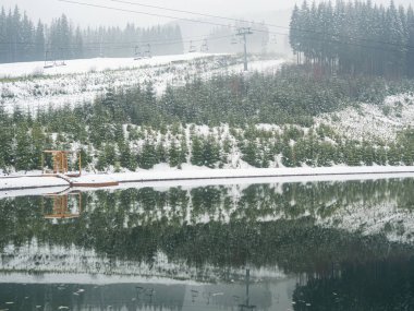 Karpatlar, Ukrayna 'daki kış gölü kıyısındaki tahta iskele. Bulutlu bir günde kozalaklı ormanlı manzaralar. Bukovel 'in modern popüler kayak merkezinin manzarası. Kışın Bukovel yakınlarında. 