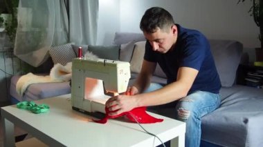 El yapımı sanayide deneyimli genç bir işçi dikiş makinesine kırmızı kumaş dikiyor, Noel Baba kırmızı şapkası üretiyor. Ev yapımı dikiş. Çalışan terzi. Noel şapkası. Kapat..