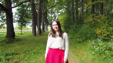 Genç kız uzun siyah saçları düzeltir. Gri kazaklı ve kırmızı etekli güzel bir kadın güneşli bir sonbahar gününde ormanda poz veriyor. Ormanda yürüyor ve dinleniyorum..