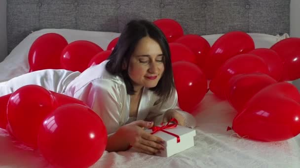 Жінка Тримає Подарунковий Ящик Між Кульками Червоної Серцевої Форми Ліжку — стокове відео
