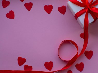 Bir sürü kalp şeklinde kâğıt, beyaz hediye kutusu ve mesaj için yeri olan düz bir yerde yatıyordu. Kırmızı kalp kağıdı arka planında hediye kutusu var. Tebrik kartı, hediye. Sevgililer Günü tatili konsepti. 14 Şubat.