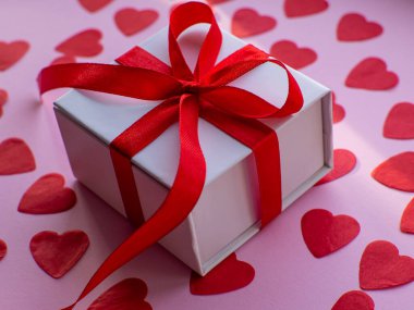 Beyaz hediye kutusu kırmızı kalp kâğıdında, üst tarafta. Tebrik kartı, hediye. Sevgililer Günü tatili konsepti. Bir sürü kalp şeklinde kâğıdı ve yazı için yeri olan düz bir yer. 14 Şubat.