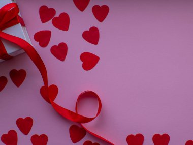 Bir sürü kalp şeklinde kâğıt, beyaz hediye kutusu ve mesaj için yeri olan düz bir yerde yatıyordu. Kırmızı kalp kağıdı arka planında hediye kutusu var. Tebrik kartı, hediye. Sevgililer Günü tatili konsepti. 14 Şubat.