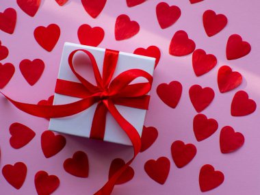 Beyaz hediye kutusu kırmızı kalp kâğıdında, üst tarafta. Tebrik kartı, hediye. Sevgililer Günü tatili konsepti. Bir sürü kalp şeklinde kâğıdı ve yazı için yeri olan düz bir yer. 14 Şubat.