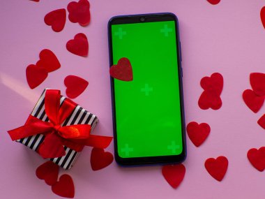 Krom ekranlı telefon ve pembe arka planda kredi kartı. Pastel pembe arka plan üzerine kırmızı kalp kağıdı, fotokopi alanı ile üst manzara. Tebrik kartı. Sevgililer Günü alışveriş konsepti. 14 Şubat. 