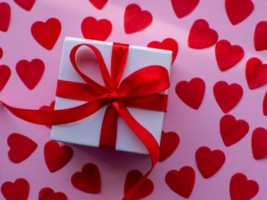 Beyaz hediye kutusu kırmızı kalp kâğıdında, üst tarafta. Tebrik kartı, hediye. Sevgililer Günü tatili konsepti. Bir sürü kalp şeklinde kâğıdı ve yazı için yeri olan düz bir yer. 14 Şubat.