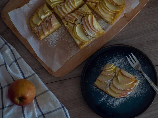 stock image Apple vanilla squares. Homemade apple pie topped with slices of apples. Serving of delicious fruit vanilla cake on a dark plate with fork. Thin slices of apples are stuffed tightly and powdered sugar.