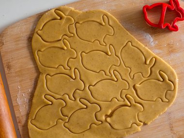 Yakından yoğurulmuş zencefil hamuru ve oyulmuş heykelcikler. Tavşan şekilleri. Paskalya şekilli kurabiye kesicilerle şekerli kurabiye hamuru kesmek. Paskalya hazırlığı. Tatil pişirme.