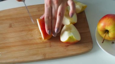 Elleri kesme tahtasındaki bir bıçakla sulu taze bir elmayı dilimler. Kadın elleri kırmızı elmayı parçalara ayırıyor. Kapatın. Ev yapımı elmalı pasta için elma kesiyorum. Ev hanımı evde taze salata yapıyor..