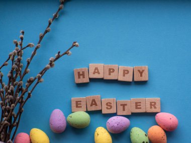 Mutlu Paskalyalar. Fotokopi alanı olan mavi arkaplanda Paskalya süslemeleri. Paskalya tebrik kartı. Düz yatıyordu. Renkli yumurtalar ve tahta küplere yazılan Mutlu Paskalyalar. Bahar tatilinin kutlaması.