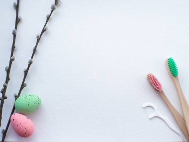 Mutlu Paskalyalar ve dişçi konsepti. Beyaz arka planda Paskalya süslemeleri olan tahta diş fırçaları. Dişçi Paskalya tebrik kartı ve fotokopi alanı. Üst manzara, düz yatış. Diş fırçası, yumurta ve diş ipi.