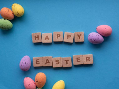 Mutlu Paskalyalar. Fotokopi alanı olan mavi arkaplanda Paskalya süslemeleri. Paskalya tebrik kartı. Düz yatıyordu. Renkli yumurtalar ve tahta küplere yazılan Mutlu Paskalyalar. Bahar tatilinin kutlaması.