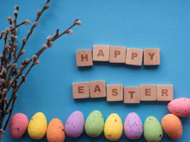 Mutlu Paskalyalar. Fotokopi alanı olan mavi arkaplanda Paskalya süslemeleri. Paskalya tebrik kartı. Düz yatıyordu. Renkli yumurtalar ve tahta küplere yazılan Mutlu Paskalyalar. Bahar tatilinin kutlaması.