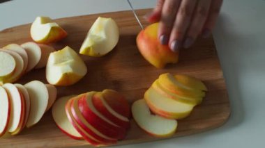 Elleri kesme tahtasındaki bir bıçakla sulu taze bir elmayı dilimler. Kadın elleri kırmızı elmayı parçalara ayırıyor. Kapatın. Ev yapımı elmalı pasta için elma kesiyorum. Ev hanımı evde taze salata yapıyor..