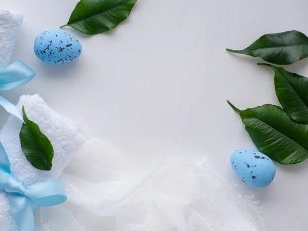 Wellness Easter concept. Set white towels tied with a ribbon in a bow, blue eggs, green leaves and copy space. White Easter card. Rolled towels in spa salon. Spa and relaxation as a gift for holidays.