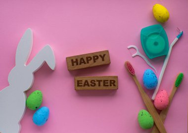 Mutlu Paskalyalar ve dişçi konsepti. Pembe arka planda Paskalya süslemeleri olan tahta diş fırçaları. Dişçi Mutlu Paskalyalar kartı. Düz yatıyordu. Diş fırçası, renkli yumurta, tavşan ve diş ipi..