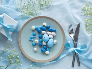 Çiçeklerle süslü Paskalya sofrası, mavi arka planda boyanmış yumurtalar ve hediye kutusu. Zarif pastel ve mavi masa manzaraları. Paskalya kutlaması. Hassas Paskalya kompozisyonu. Yukarıdan görüntüle