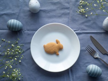 Mavi arka planda çiçekler, yumurtalar ve tavşan şekilli kurabiyeli Paskalya sofrası. Zarif masa manzaraları. Paskalya kutlaması. Hassas Paskalya kompozisyonu. Yukarıdan görüntüle.