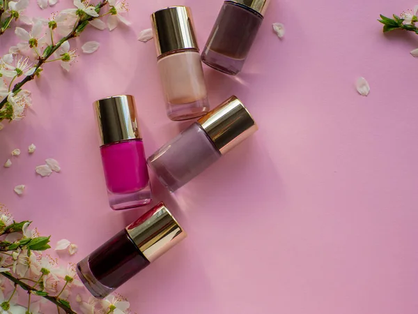Set of cosmetic nail polishes on pink background with cherry flowers and copy space. Women and Mothers Day gift. Concept of beauty and femininity. Buying gifts online.