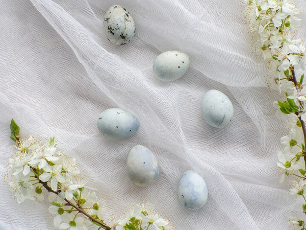 Blue painted easter eggs. Dyed Easter eggs with marble stone effect light blue color on white tablecloth background with cherry blossom. Eggs background with copy space, Ester holiday postcard concept