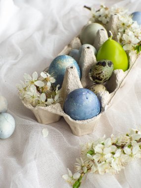 Mavi boyalı Paskalya yumurtaları ve tepside mum. Mermer efektli boyanmış Paskalya yumurtaları kiraz çiçekli beyaz masa örtüsünün üzerine açık mavi renk. Kopya alanı olan yumurta arkaplanı, tatil kartı kavramı.